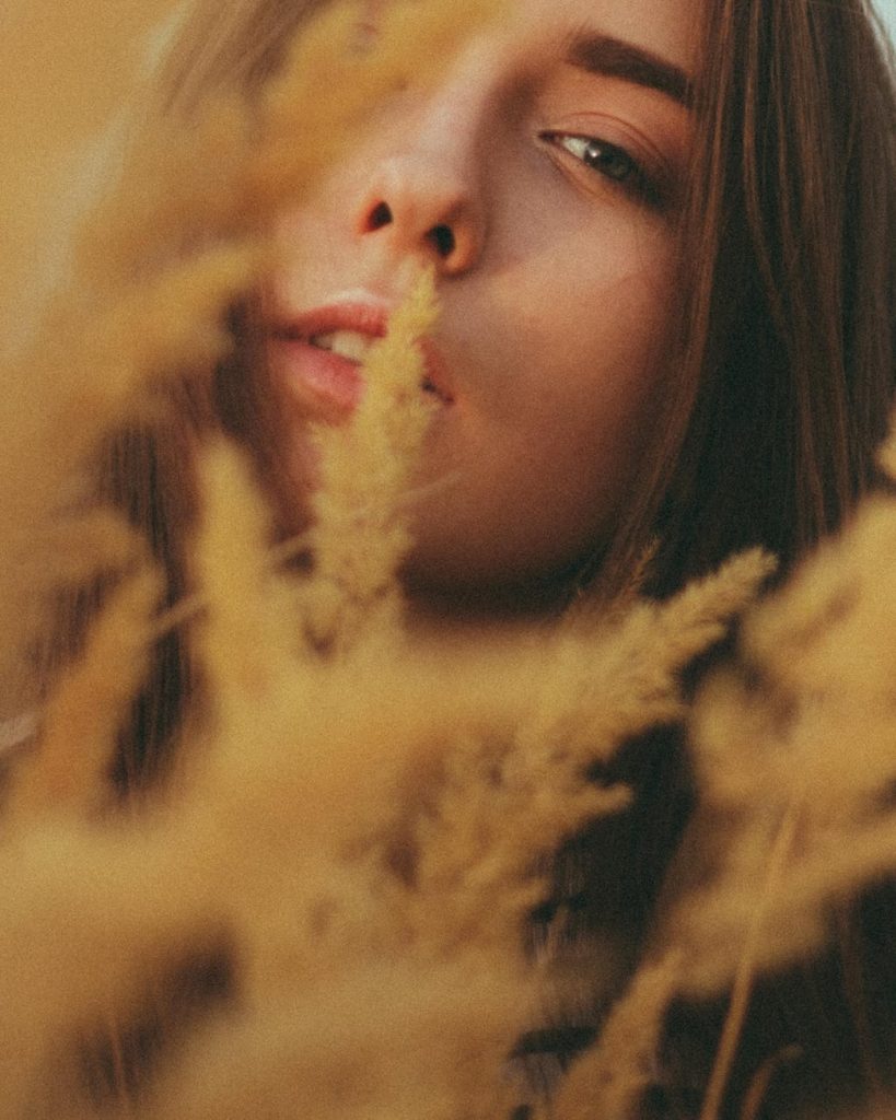 calm young woman looking at camera through tall reeds in nature